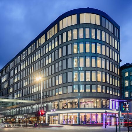 Yotel Glasgow Exterior foto The photo shows a modern office building with a distinctive curved shape and a facade made of large glass windows. It is illuminated against a twilight sky, giving it a contemporary appearance. The ground floor features large glass entrance areas, li